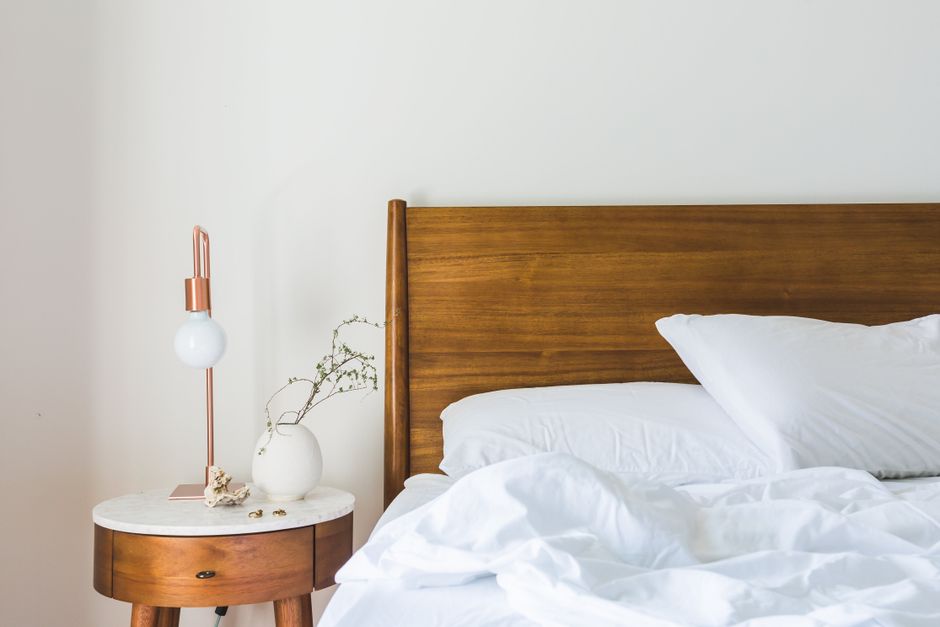 A professional cleaner from Purley Carpet Cleaners, dressed in protective clothing and a face mask, is performing surface cleaning and sanitisation of a mattress using a vacuum attachment. The scene i